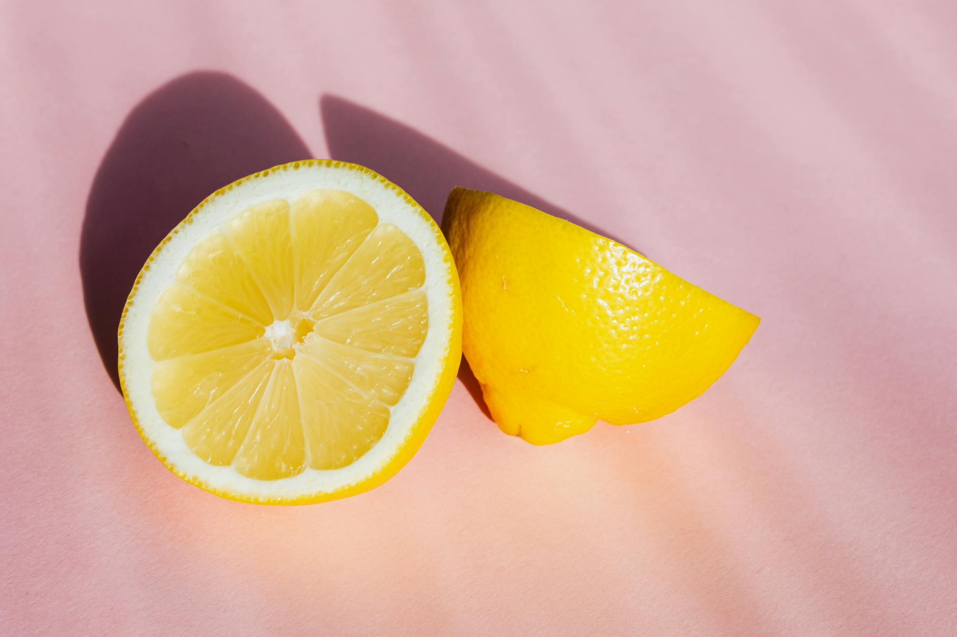 Hand holding a fresh lemon against soft pink background, symbolizing gentle and natural wellness.