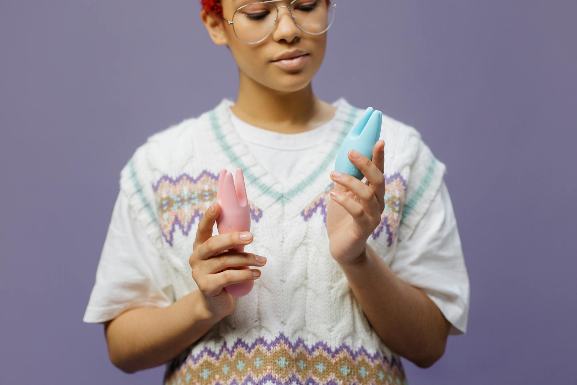 Woman holding blue and pink clitoral vibrators in contemplative moment after stopping hormonal birth control
