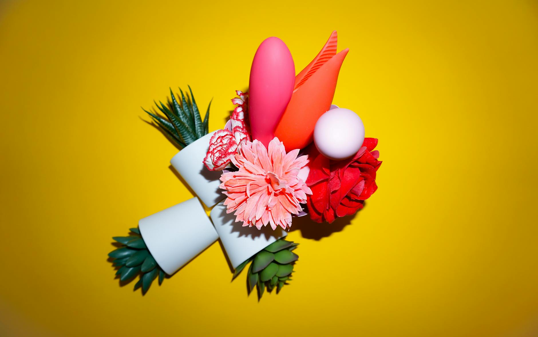 Hands holding pink and blue silicone vibrators against a pastel background