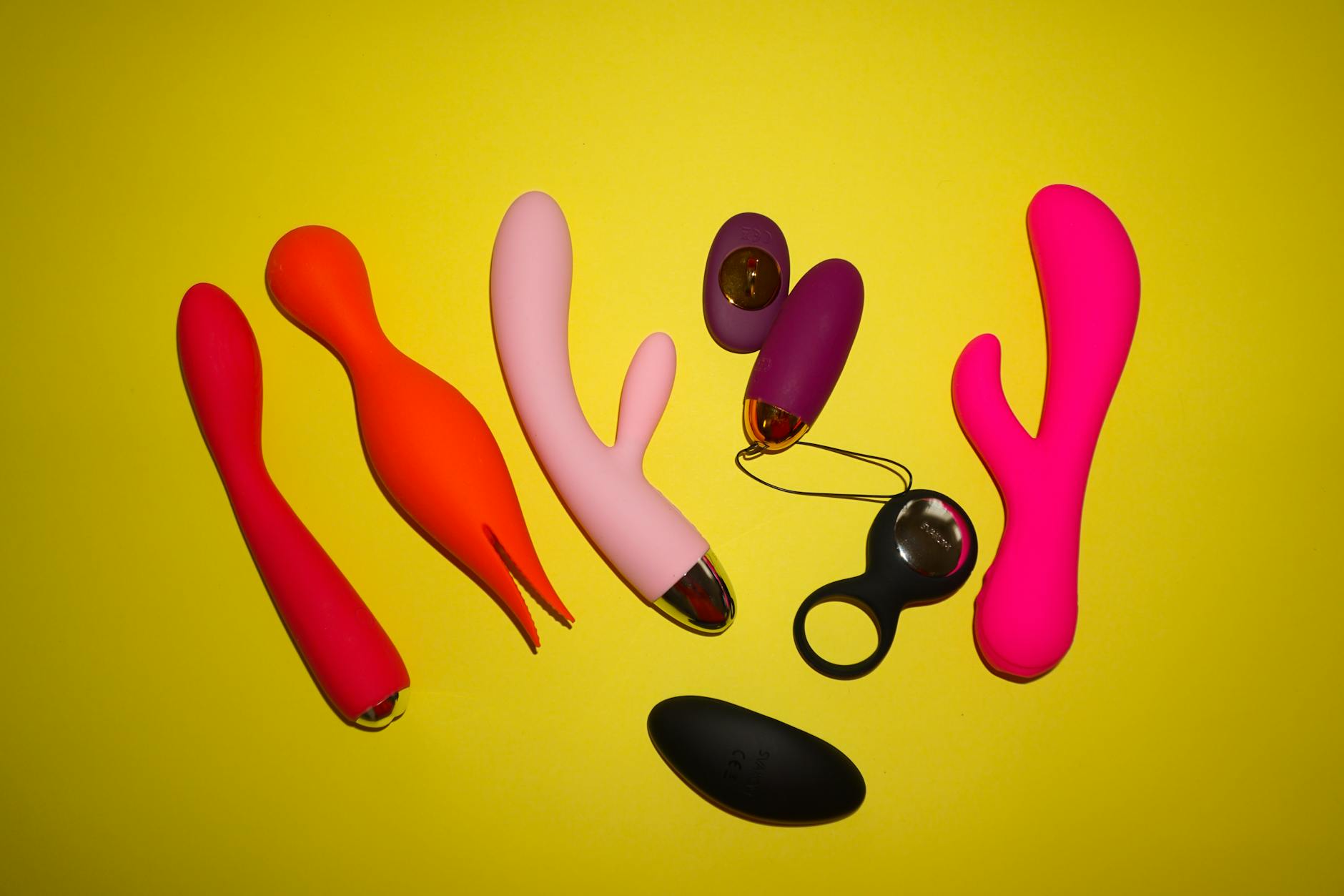 Colorful vibrators and toys arranged on a bright yellow surface