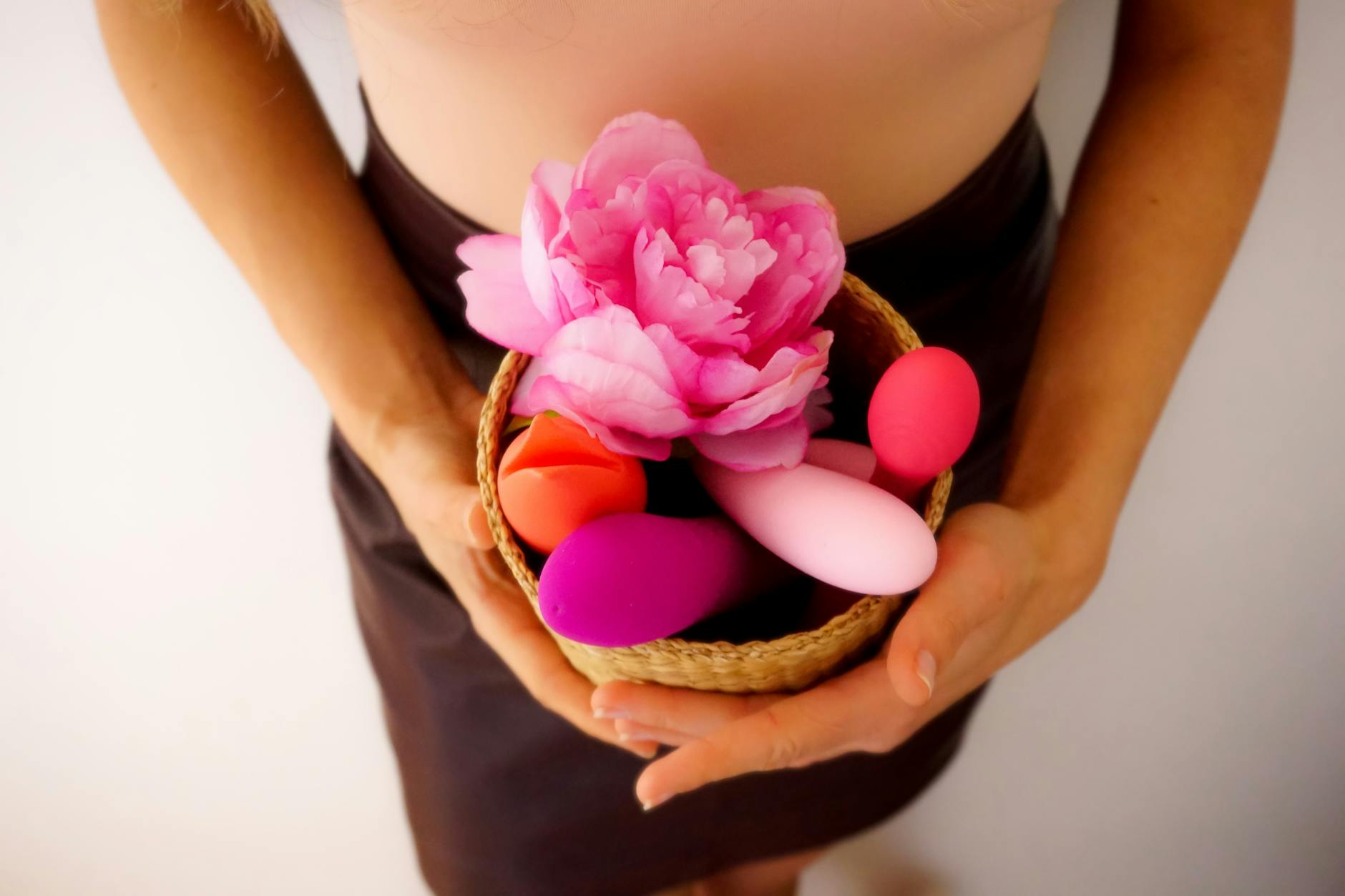 A basket of colorful vibrators and toys arranged with fresh flowers on a bright background